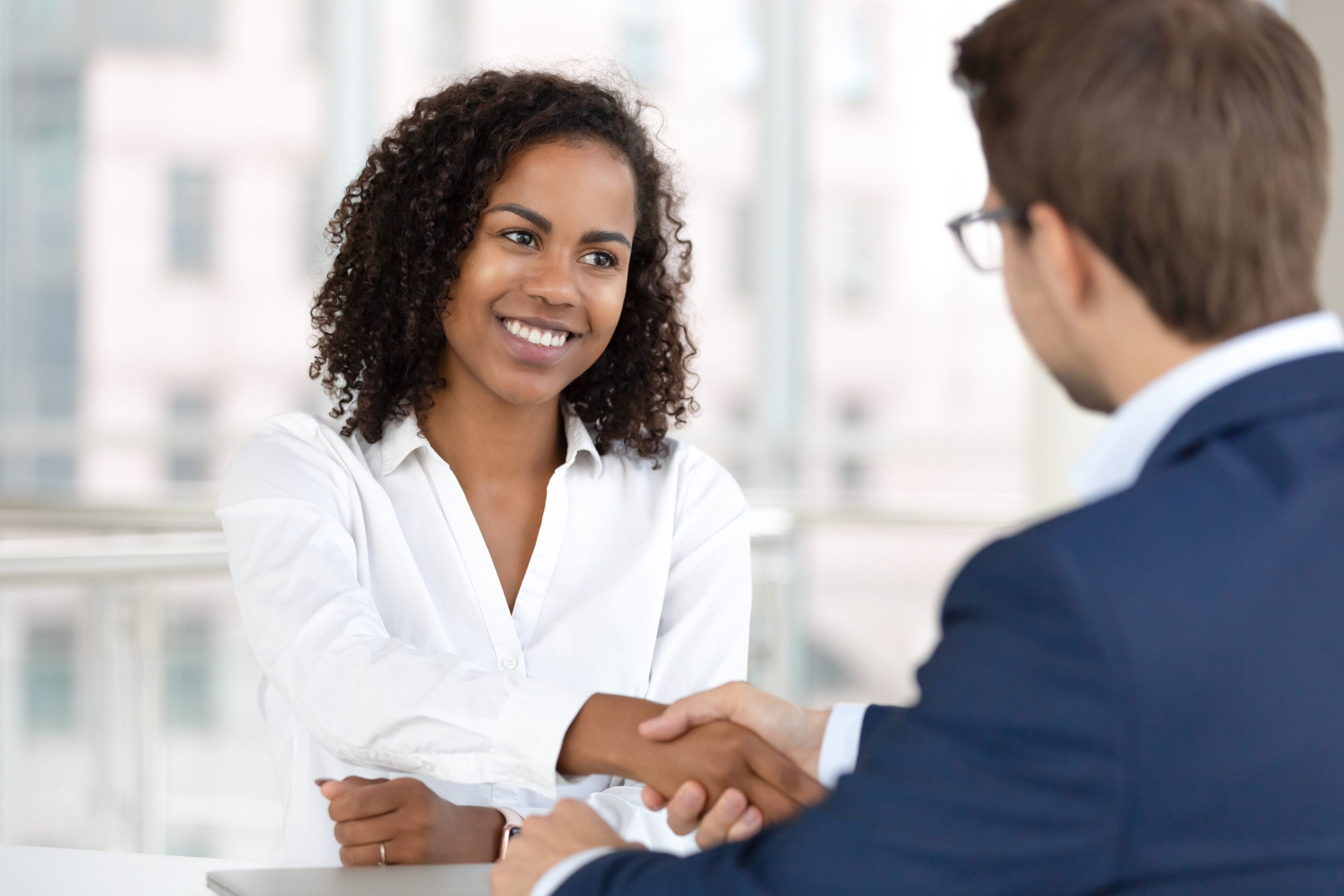 Smiling african female hr manager handshake hire male candidate at job interview make good first impression, happy mixed race client shake hand of bank broker, respect, business agreement concept